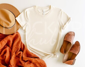 May include: A beige t-shirt with rolled up sleeves, a brown hat, a rust-colored blanket, and two pairs of brown sandals on a white background.