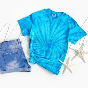 May include: A blue tie-dye t-shirt with a white background and a pair of blue denim shorts.  There are two white starfish on the white background.