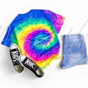 May include: A tie-dye t-shirt with a rainbow swirl pattern, blue denim shorts, and black canvas sneakers.
