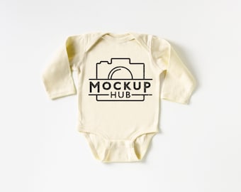 May include: A cream colored long-sleeved baby onesie with a black camera graphic and the text "MOCKUP HUB" printed on the front.