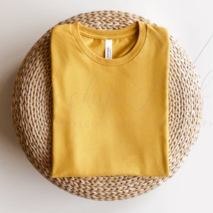 May include: A mustard yellow t-shirt folded on a woven round mat.