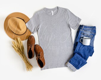 May include: A flat lay of a gray t-shirt, blue jeans, brown boots, a brown hat, and wheat stalks on a white background.