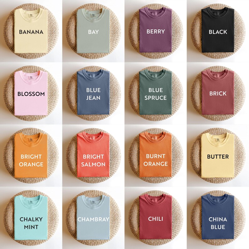 May include: A collection of sixteen t-shirts in various colors, including yellow, green, purple, and black. Each shirt is displayed on a round, woven surface. The shirts have text labels such as "Banana," "Bay," and "Berry."