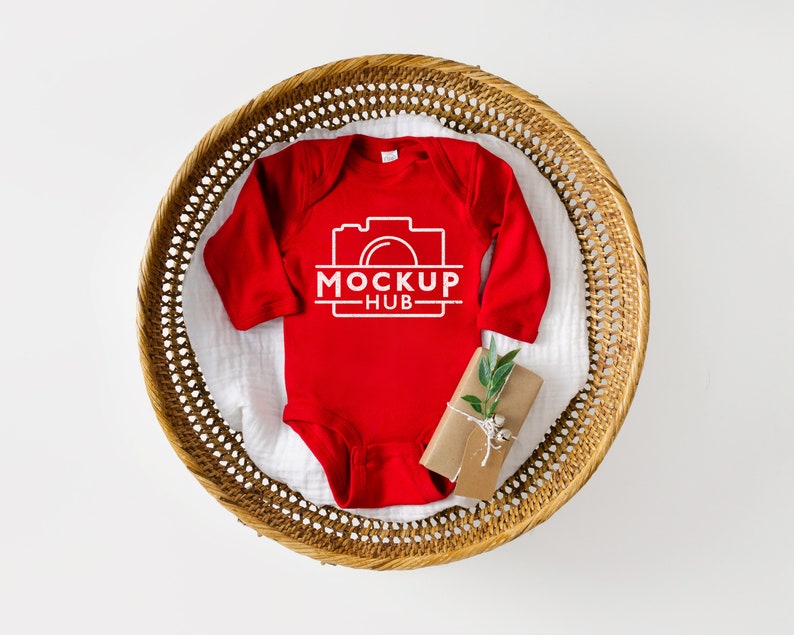 K&ouml;nnte beinhalten: Roter Langarm-Babybody mit einer wei&szlig;en Kamera-Grafik und dem Text "MOCKUP HUB". Der Body liegt in einem geflochtenen Korb.