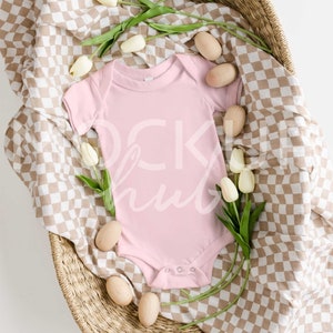 May include: A pink baby onesie in a wicker basket with a checkered brown and white blanket, white tulips, and wooden eggs.