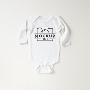 May include: White long-sleeve baby onesie with a black camera graphic and the text "MOCKUP HUB" printed on the front.