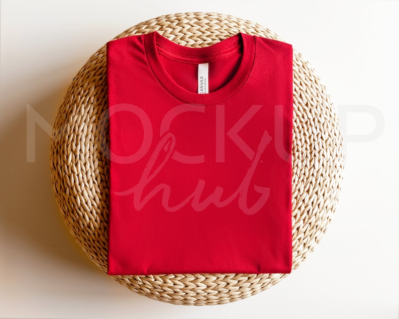 May include: A red t-shirt folded on a woven round mat. The t-shirt is a blank canvas for customization.