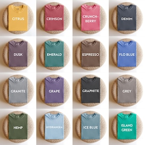 May include: A collection of folded t-shirts in various colors, including Citrus, Crimson, Crunch-Berry, and Denim. Each shirt is displayed on a round, woven mat. The shirts have the color name printed on them in white.