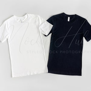 May include: Two blank t-shirts, one white and one black, laid flat on a gray surface.