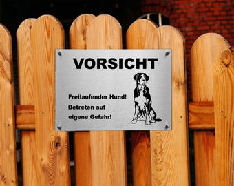 Könnte beinhalten: Ein silbernes Metallschild mit schwarzem Text, der "Vorsicht Freilaufender Hund! Betreten auf eigene Gefahr!" lautet. Das Schild zeigt außerdem eine Schwarzweißillustration eines Hundes.