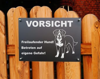 Könnte beinhalten: Schwarzes rechteckiges Schild mit weißem Text und Hundeillustration, montiert an einem Holzzaun. Das Schild trägt oben die Aufschrift "VORSICHT", darunter weiterer Text, der vor einem freilaufenden Hund warnt. Die Hundeillustration ist eine Schwarz-Weiß-Umrisszeichnung.
