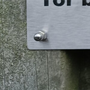 May include: A close-up of a silver metal screw with a rounded head, attached to a silver metal surface.