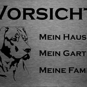 May include: A black and white sign with the text "Vorsicht" at the top. Below the text is a silhouette of a dog's head. The text "Mein Haus", "Mein Garten", and "Meine Familie" are printed below the dog's head.