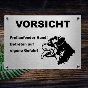 May include: A white sign with black text and a black silhouette of a dog's head. The sign reads "Vorsicht Freilaufender Hund! Betreten auf eigene Gefahr!" which translates to "Caution Free-running Dog! Enter at your own risk!"