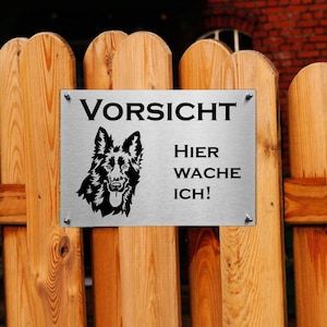 Könnte beinhalten: Ein silbernes Metallschild mit schwarzem Text und einer schwarzen Silhouette eines Deutschen Schäferhundes. Das Schild lautet "Vorsicht Hier Wache Ich!"