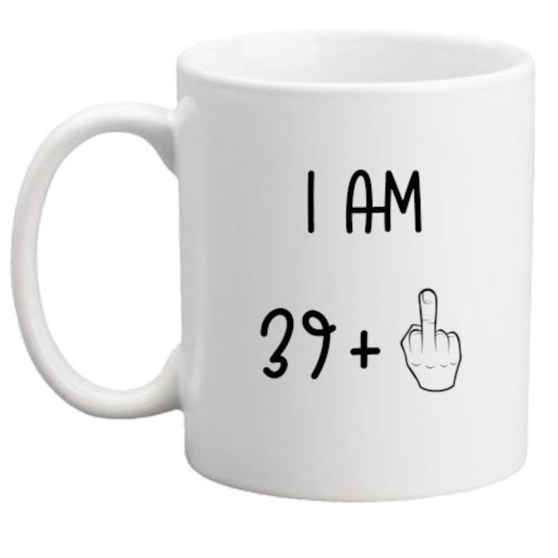 May include: White ceramic coffee mug with black text that reads "I am 39+" with a middle finger emoji.
