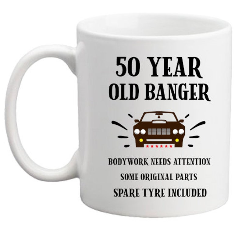May include: White ceramic mug with a black and brown illustration of a car and the text "50 Year Old Banger". The text below the car reads "Bodywork needs attention, some original parts, spare tyre included."