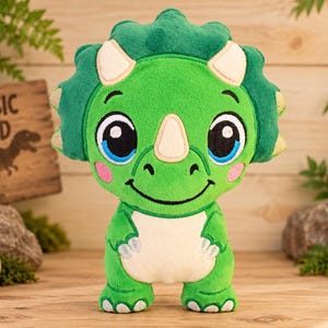 Pode incluir: Um peluche de dinossauro triceratops verde com uma cabeça grande, chifres cor de creme e uma barriga branca. O brinquedo apresenta detalhes faciais bordados, incluindo olhos grandes azuis e pretos, uma boca sorridente e bochechas rosadas.