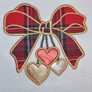 May include: Embroidered bow with a red tartan pattern and gold edging. Three hanging hearts in red, gold, and silver are below the bow. The design is on a white background, suitable for crafts or embellishments.