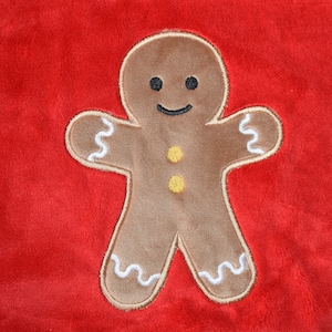 May include: A brown gingerbread man with a smiling face, yellow buttons, and white icing details is embroidered on a red background. The festive design is perfect for holiday decorations or seasonal crafts.