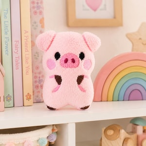 May include: A small, plush pig toy with soft light pink fabric, embroidered black eyes, a pink snout, and dark brown accents on the feet and arms. The pig has rounded ears and pink circular patches on its cheeks, standing upright as a stuffed animal.