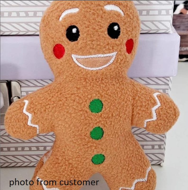 Op de afbeelding: Een zacht gingerbread man speelgoed met een lachend gezicht, zwarte ogen en rode wangen. De gingerbread man heeft groene knoopaccenten en witte glazuurdetails. De tekst "photo from customer" is zichtbaar onderaan de afbeelding.