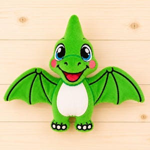 May include: A plush pterodactyl toy featuring bright green fabric, a white belly patch, and large blue eyes. The creature has a pointed head crest, outstretched wings with black embroidered details, a smiling mouth, and pink circular cheek accents.