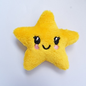 Może przedstawiać: Pluszowa żółta gwiazda z haftowanymi detalami. Posiada czarne oczy, uśmiechnięte usta i różowe policzki. Zabawka wykonana jest z miękkiego, puszystego materiału. Prawdopodobnie jest to zabawka dla dzieci lub przedmiot dekoracyjny.