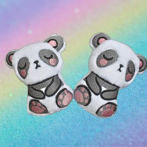 Puede incluir: Dos parches bordados de osos panda. Los pandas son blancos con detalles grises, ojos negros y orejas y patas rosas. Los parches est&aacute;n dise&ntilde;ados para parecer pandas durmiendo. El fondo es un degradado de azul, morado y rosa.