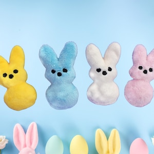 May include: Four plush bunny figures in yellow, blue, white, and pink, each with black eyes. The bunnies are arranged against a light blue background. Easter-themed decorations are at the bottom.