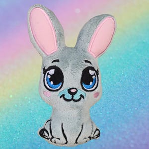 May include: A plush gray bunny with large blue eyes, pink inner ears, and a small pink nose. The bunny has a smiling face and is sitting upright. The background is a soft gradient of pastel colors.