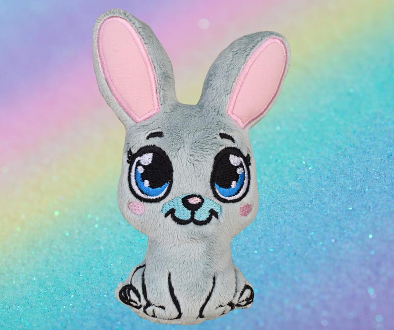 May include: A plush gray bunny with large blue eyes, pink inner ears, and a small pink nose. The bunny has a smiling face and is sitting upright. The background is a soft gradient of pastel colors.