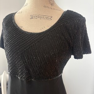 Peut inclure: Robe noire avec un corsage perl&eacute; et des manches courtes. Le corsage pr&eacute;sente des motifs perl&eacute;s diagonaux et horizontaux. La robe a une encolure d&eacute;gag&eacute;e et une jupe noire unie. La robe est pr&eacute;sent&eacute;e sur un mannequin.