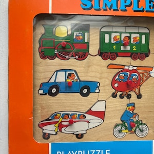 Puede incluir: Rompecabezas de madera Simple Playpuzzle con un tren, un coche, un helicóptero, un avión y una bicicleta. El tren es verde, el coche es azul, el helicóptero es rojo, el avión es blanco y rojo, y la bicicleta es verde. La caja es naranja y azul.