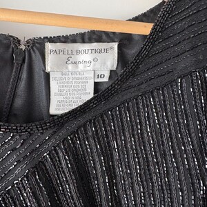 Peut inclure: Gros plan d'une robe de soir&eacute;e noire avec des franges perl&eacute;es et un d&eacute;collet&eacute; perl&eacute;. La robe porte une &eacute;tiquette &laquo; PAPELL BOUTIQUE Evening &raquo; et la taille 10. La robe est en soie et polyester.