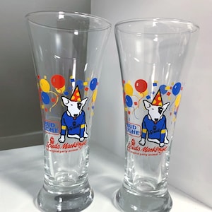 May include: Two clear glass Bud Light beer glasses with a cartoon dog wearing a party hat and a blue sweater. The glasses have red, yellow, and blue balloons and confetti printed on them. The text on the glasses reads "Bud Light" and "Spuds Mackenzie, the original party animal."