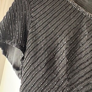 Peut inclure: Gros plan d'un haut noir &agrave; perles avec un d&eacute;collet&eacute; en V et des manches courtes. Le tissu est textur&eacute; avec des rang&eacute;es diagonales de perles, cr&eacute;ant un effet scintillant. L'encolure est &eacute;galement orn&eacute;e de perles.