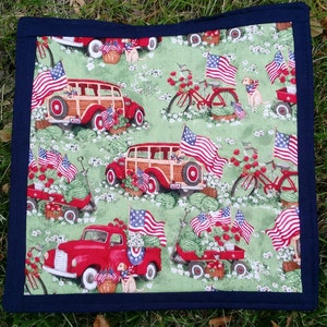 May include: A red, white, and blue patriotic themed fabric placemat with a repeating pattern of vintage cars, bicycles, and American flags. The placemat has a dark blue border.