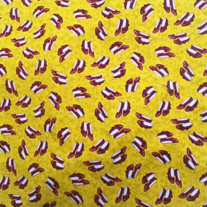 May include: Yellow fabric with a repeating pattern of maroon and white high heels. The heels are arranged randomly across the surface, creating a playful and fashionable design. The background is a solid yellow color.