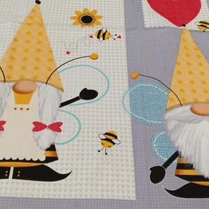 May include: A fabric panel featuring two whimsical bee gnome designs. The gnomes have yellow and black striped bodies, white beards, and yellow hats. They are adorned with red bow ties and blue wings, surrounded by bees and hearts.