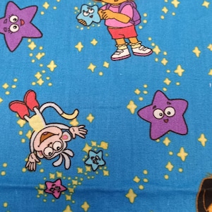 May include: Blue fabric featuring Dora the Explorer and Boots the monkey, along with purple and pink stars. The design includes yellow starbursts, creating a playful and whimsical pattern. The fabric is suitable for children's crafts and apparel.