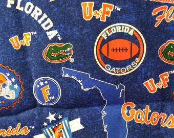 Może przedstawiać: Niebieski materiał z powtarzającym się wzorem logo Florida Gators, w tym maskotki aligatora, nazwy drużyny i stanu Floryda. Materiał zawiera również kolory drużyny, pomarańczowy i niebieski.