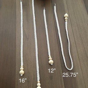 May include: Five white macrame plant hangers with wooden beads. The hangers are 12 inches, 16 inches, 19 inches, and 25.75 inches long.