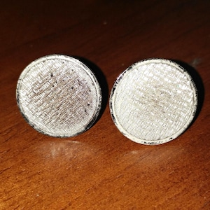 May include: A pair of silver cufflinks with a textured, patterned design.