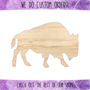 May include: A wooden cutout of a bison in a side profile. The cutout is a light brown color and has a wood grain texture.