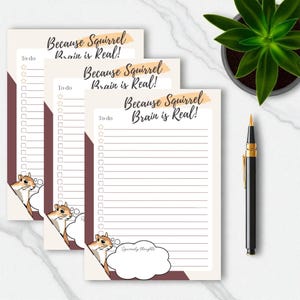 May include: Three cream-colored to-do list notepads with the text "Because Squirrel Brain is Real!" and a cartoon squirrel peeking from the corner. A black and gold pen and a potted succulent are also visible.
