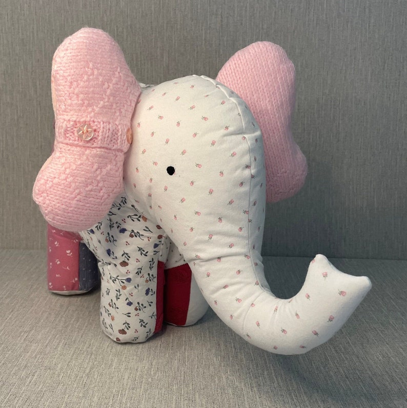 May include: A patchwork elephant stuffed animal with pink knit ears and a white body with a floral pattern. The elephant has a button on its ear.