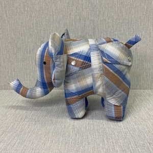 May include: A blue and brown plaid elephant stuffed animal. The elephant has a long trunk and a small tail. The fabric is a plaid pattern with blue, brown, and white squares.