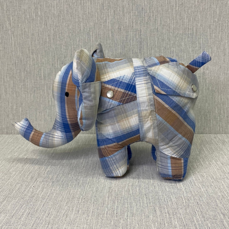 May include: A blue and brown plaid elephant stuffed animal. The elephant has a long trunk and a small tail. The fabric is a plaid pattern with blue, brown, and white squares.