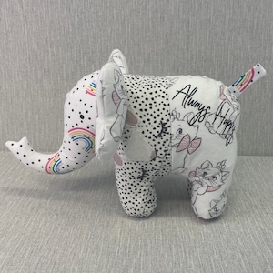 May include: A white and black patchwork elephant plush toy with a rainbow design on the trunk. The elephant has a black and white polka dot pattern on one side and a white background with a black and white cat illustration and the text "Always Happy" on the other side.